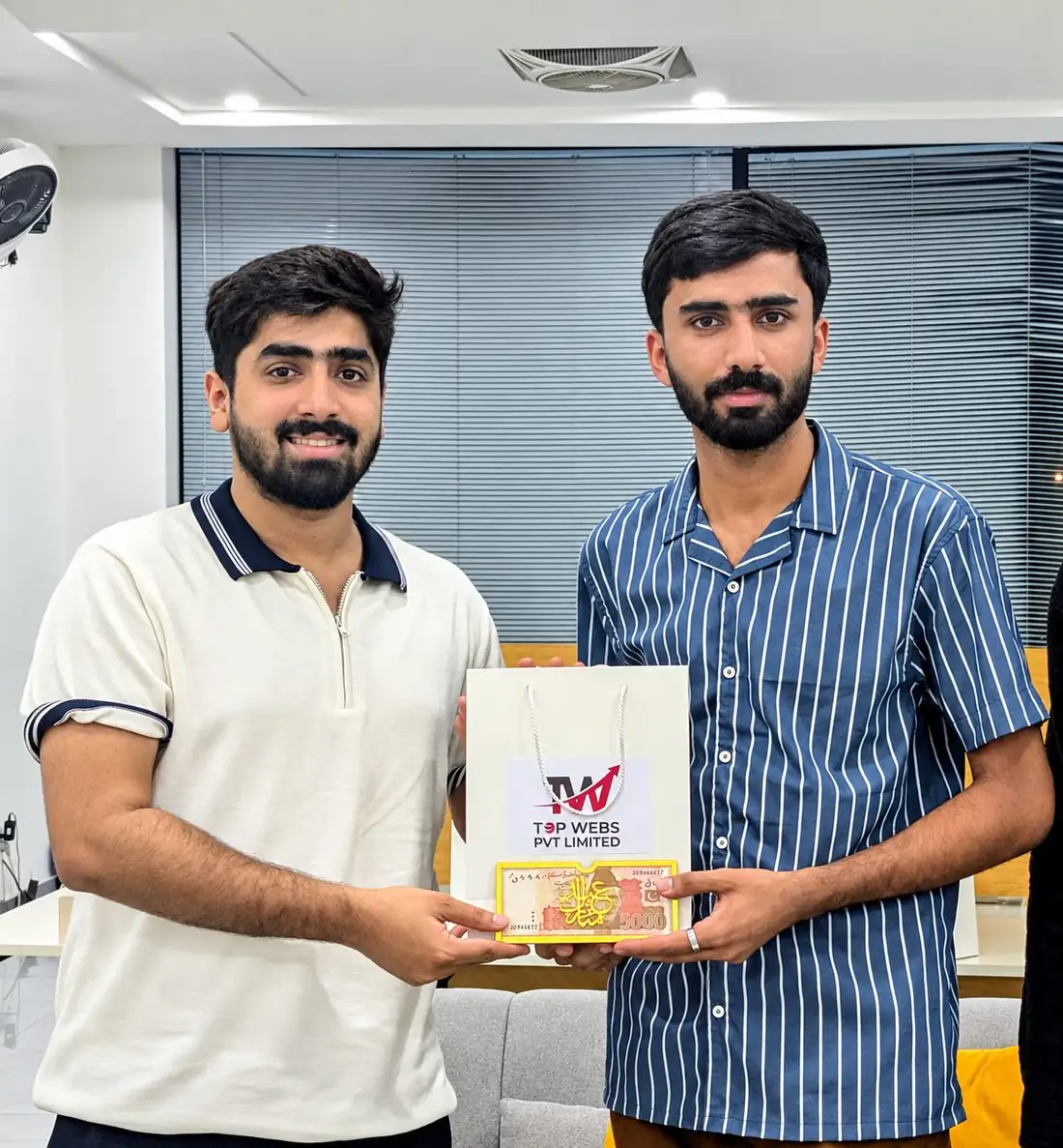 Two Topwebs team members holding a Topwebs gift bag and an Eid Mubarak Eidi envelope