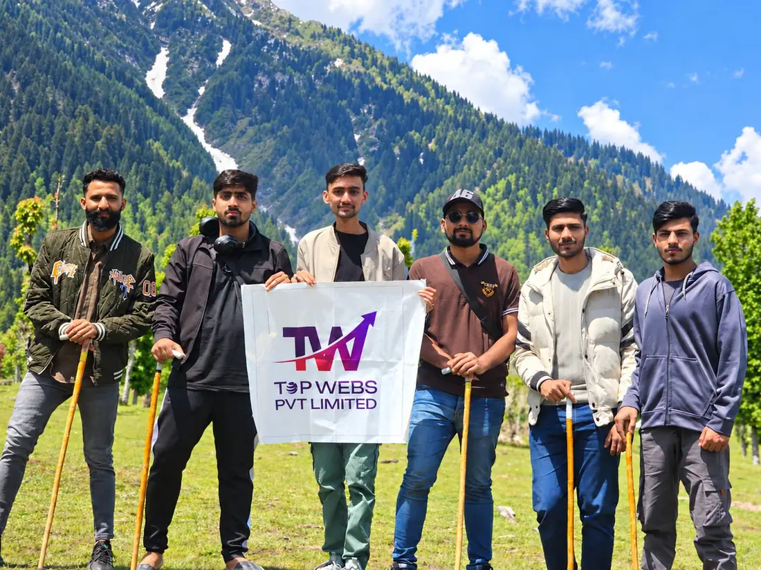 Six Topwebs team members holding the company banner in a mountain meadow